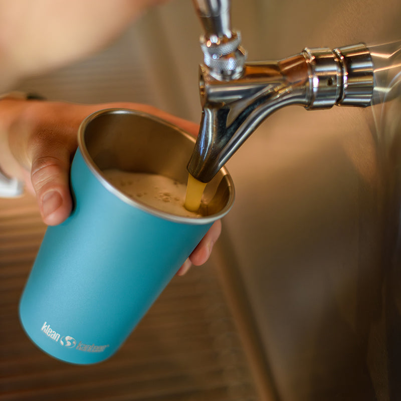 Blue steel pint cup being filled with a beverage from a tap.