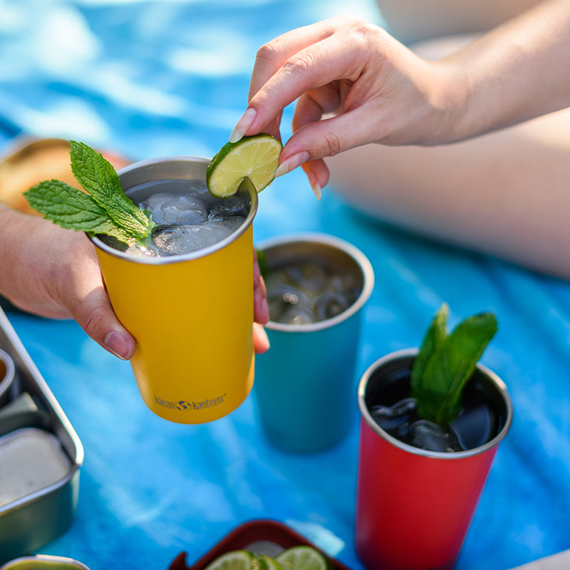 Colorful cups with cocktail drinks and garnishes on a picnic blanket