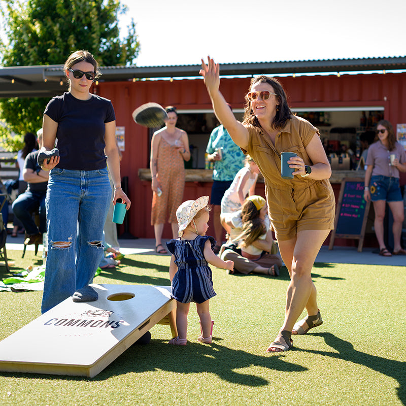 Woman playing cornhole with a child at an outdoor event.