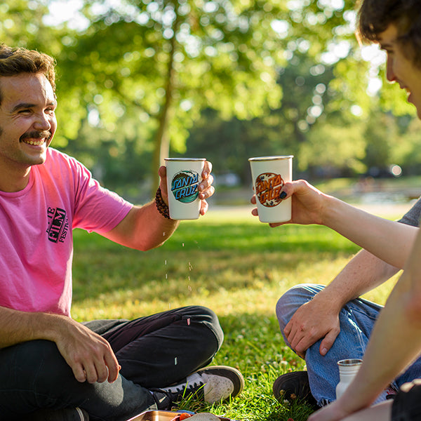 Two people sitting outdoors in a park, holding branded Santa Cruz steel cups