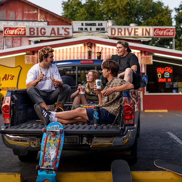 Four skateboard friends sitting in the back of a pickup truck at a drive-in restaurant. with Santa Cruz pint cups