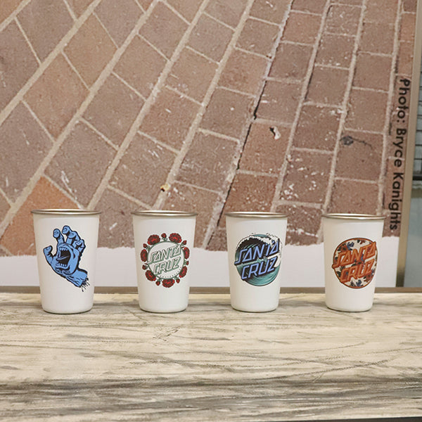 Four Santa Cruz branded pint cups on a marble surface with a brick wall background.