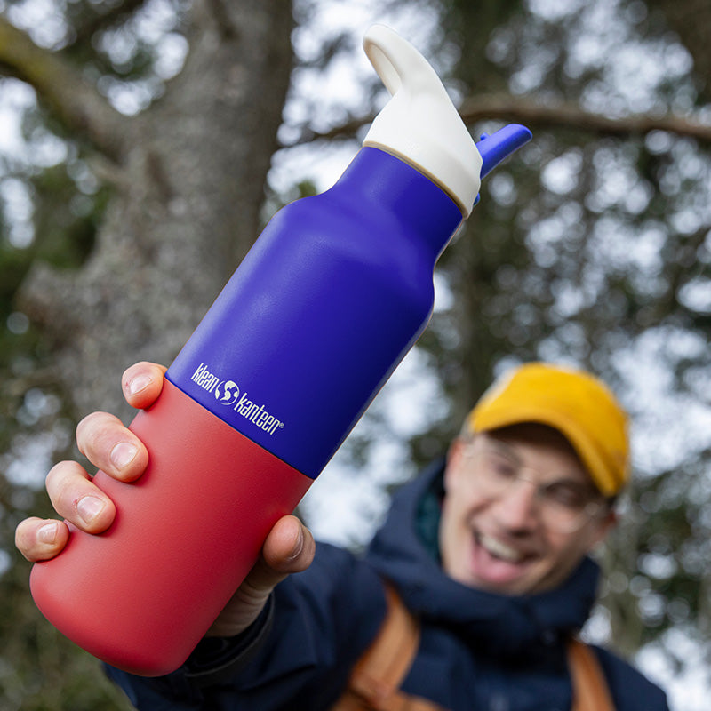 Person holding a red and blue Klean Kanteen water bottle outdoors.