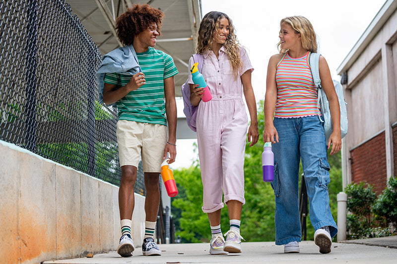 Three young teenagers walking on school campus with bright color water bottles