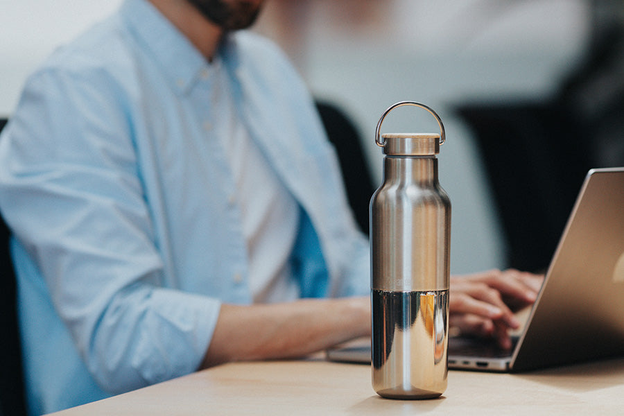 Person using a laptop with a Reflect water bottle on a desk