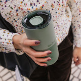 Person holding a green insulated mug with a colorful textured sweater