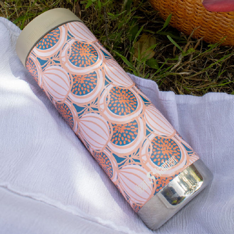 Patterned water bottle with figs on a white cloth with grass in the background
