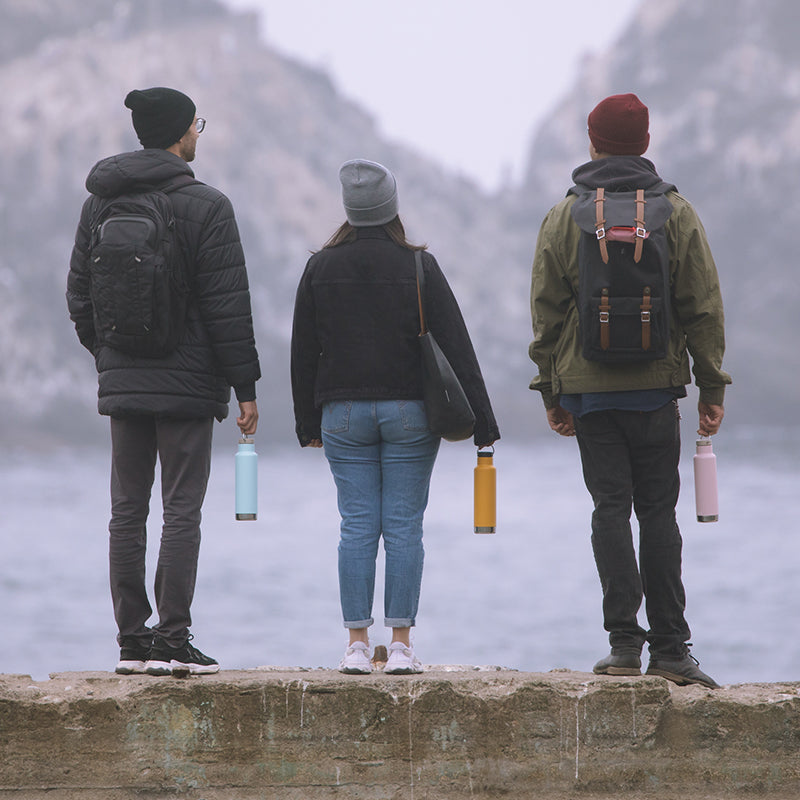 Three people with backpacks and water bottles standing on a ledge overlooking a misty landscape.