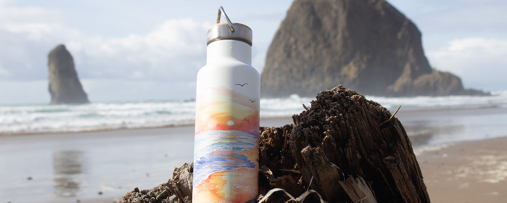 Earth Day Bottle with beach graphic, on beach driftwood stump