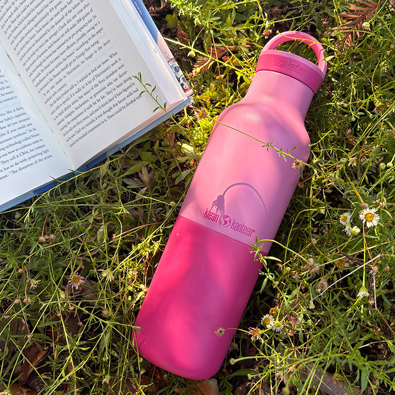 Pink water bottle on grass next to an open book