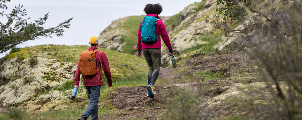 Two people hiking on a trail with backpacks and water bottles