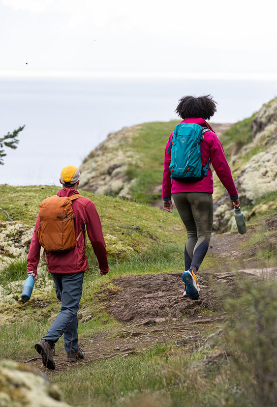Two people hiking on a trail with backpacks and water bottles