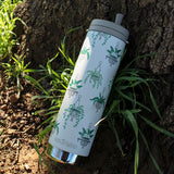 White water bottle with green plant patterns leaning against a tree trunk.