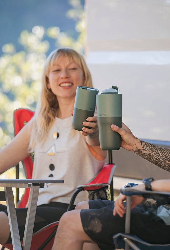 Two people toasting with tumblers in camping chairs