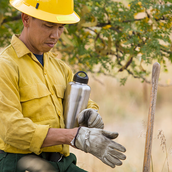 Fire fighter in hard hat and gloves holding a water bottle outdoors
