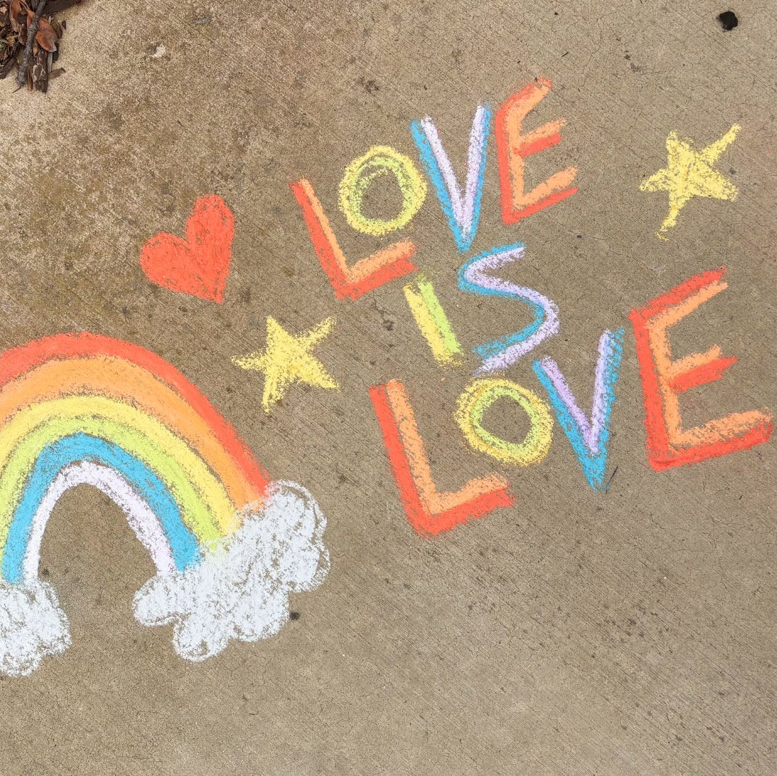 Chalk art on pavement with 'Love is Love' and a rainbow.