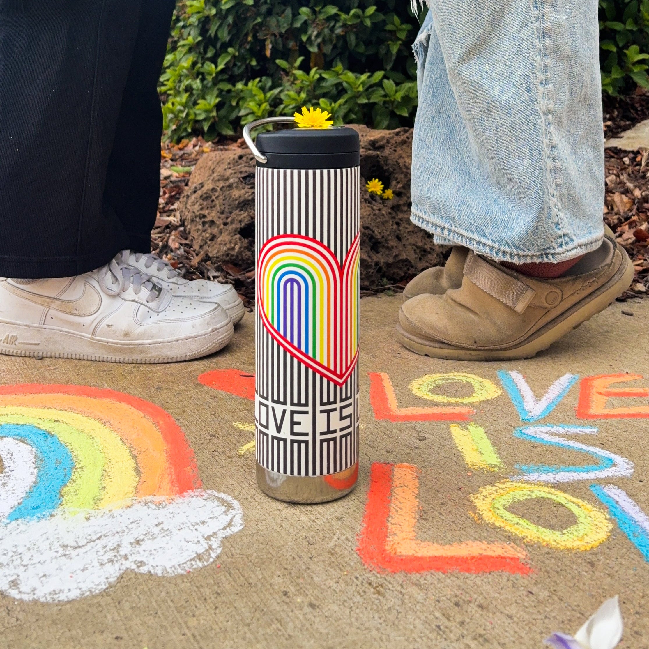Tumbler with rainbow design and 'LOVE IS LOVE' text on a ground with painted rainbows and flowers.
