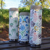 Three insulated tumblers with floral and nature-themed designs on a wooden surface outdoors.