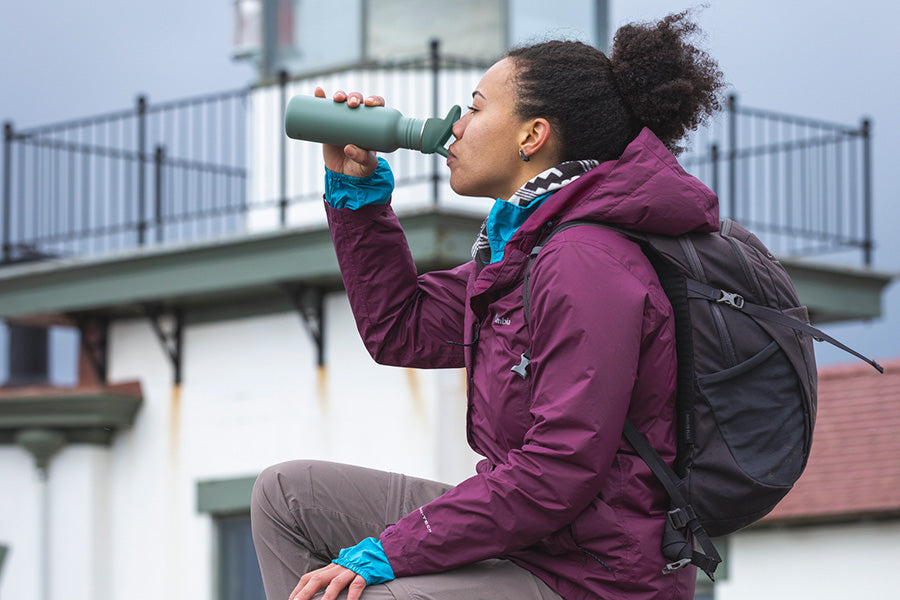 Woman drinking from water bottle in front of light house
