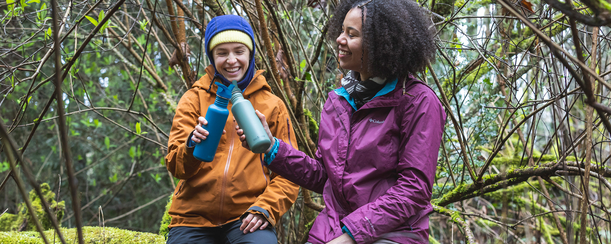 Two women hiking in woods with water bottles