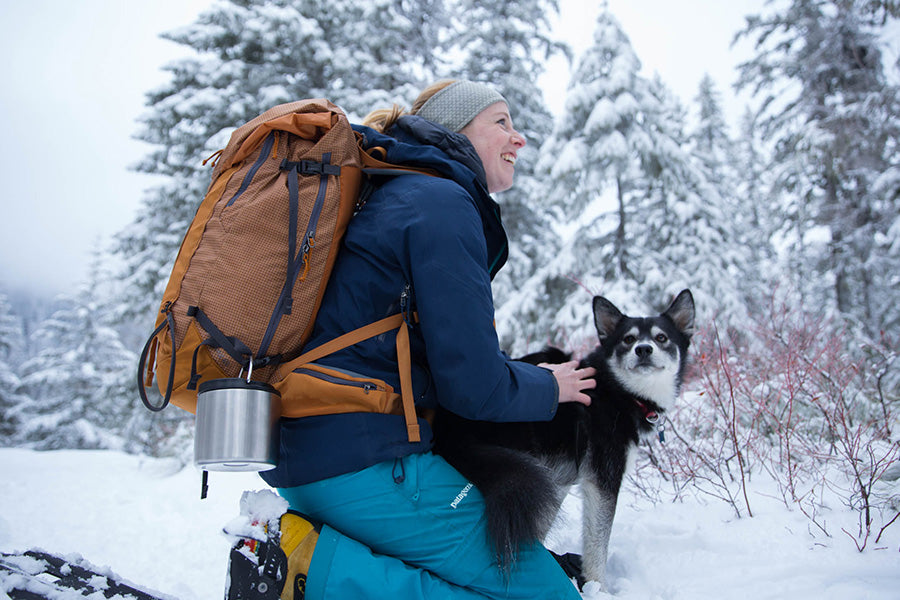 Woman snowshoeing with dog and food canister full of soup