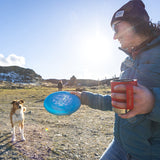 Woman with frisbee and dog drinking from coffee mug