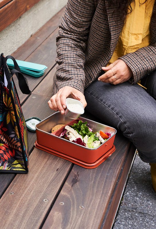 Person preparing a lunch  - pouring dressing from food container into lunch box