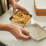 Person holding a metal lunch container with pasta salad on a marble surface