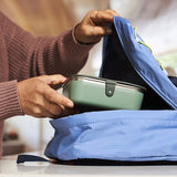 Person placing a green lunch box into a blue backpack