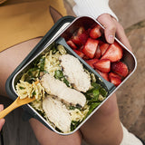 Person holding a bento food box with chicken salad and strawberries