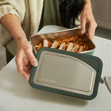 Person holding a steel lunch cbox ontainer with food on a white surface