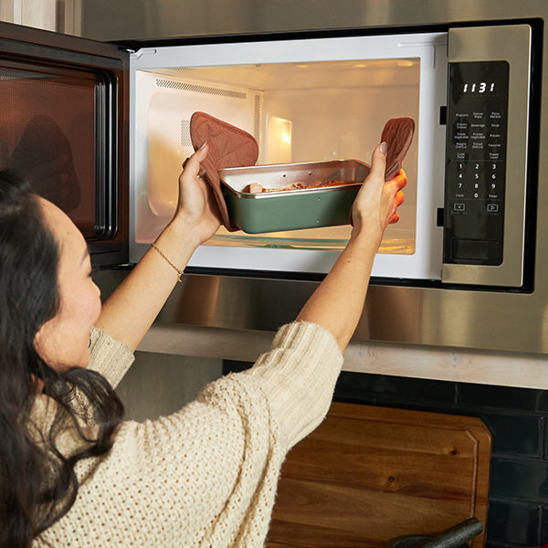 Person placing a steel lunch into a microwave oven