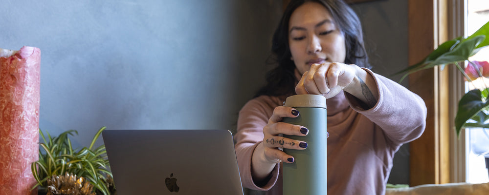 Woman holding a coffee mug with a laptop on a desk