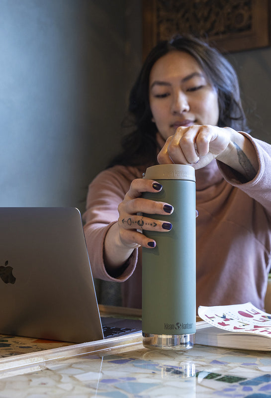Woman holding a coffee mug with a laptop on a desk