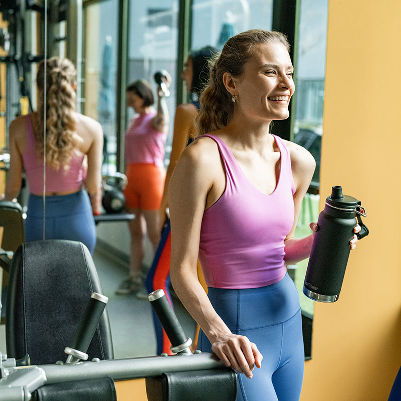 Woman in a gym holding a water bottle, smiling.